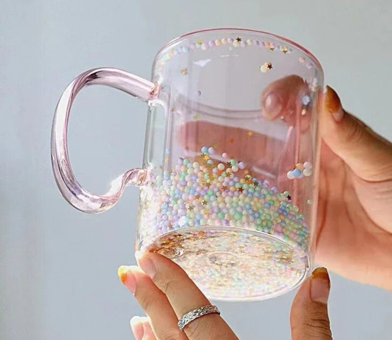 A person holding a Pink Bubble Star Glass Mug filled with sprinkles.