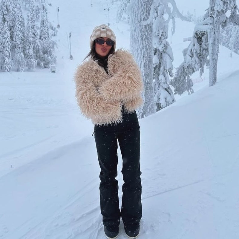 Woman in beige faux sheep jacket and sunglasses standing in snow