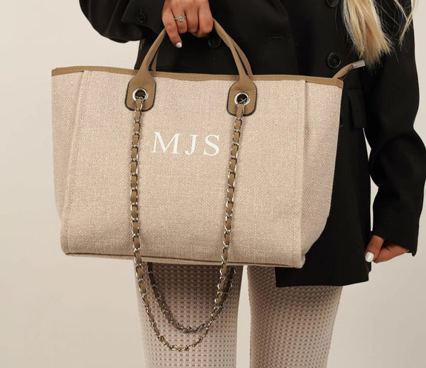 A woman holding a beige tote bag with the initials MJS. Product name: Canvas Tote Bag with Chain Beach bag- Tan/beige.
