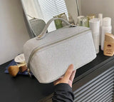 A person holding a gray cosmetic bag with handle, labeled "Large sparkle glitter make up toiletry cosmetic bag