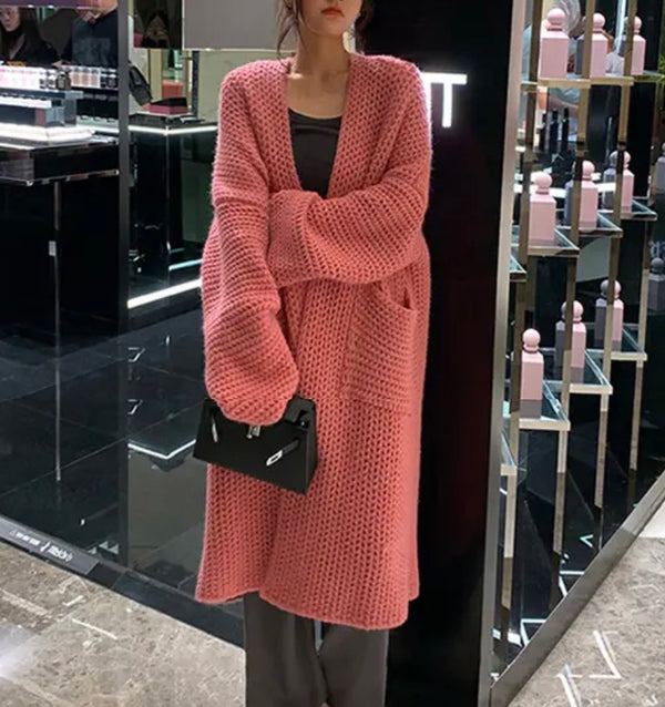 Woman wearing a pink knitted long cardigan and black pants.