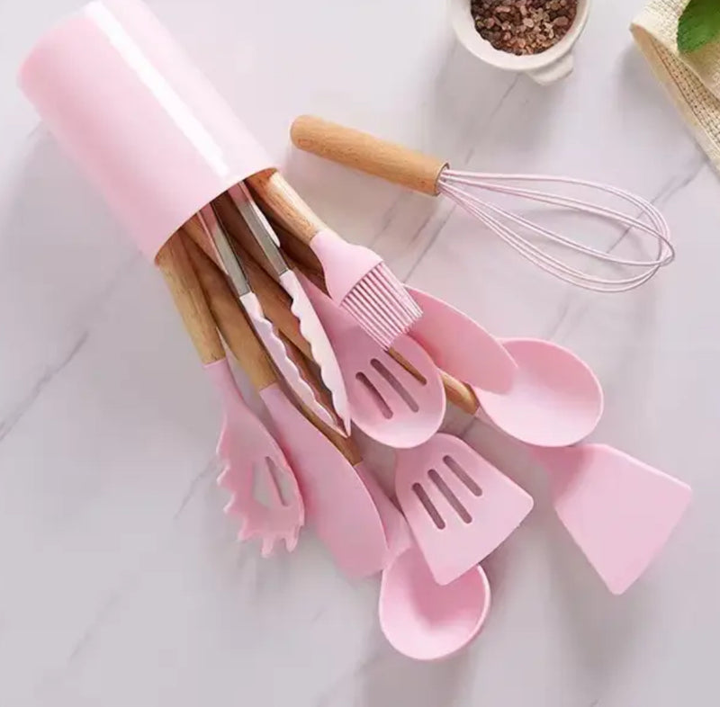 A cup filled with pink silicone kitchen utensils, including spatulas, spoons, and tongs. Product name: Pink 12Pcs Cooking Utensils.