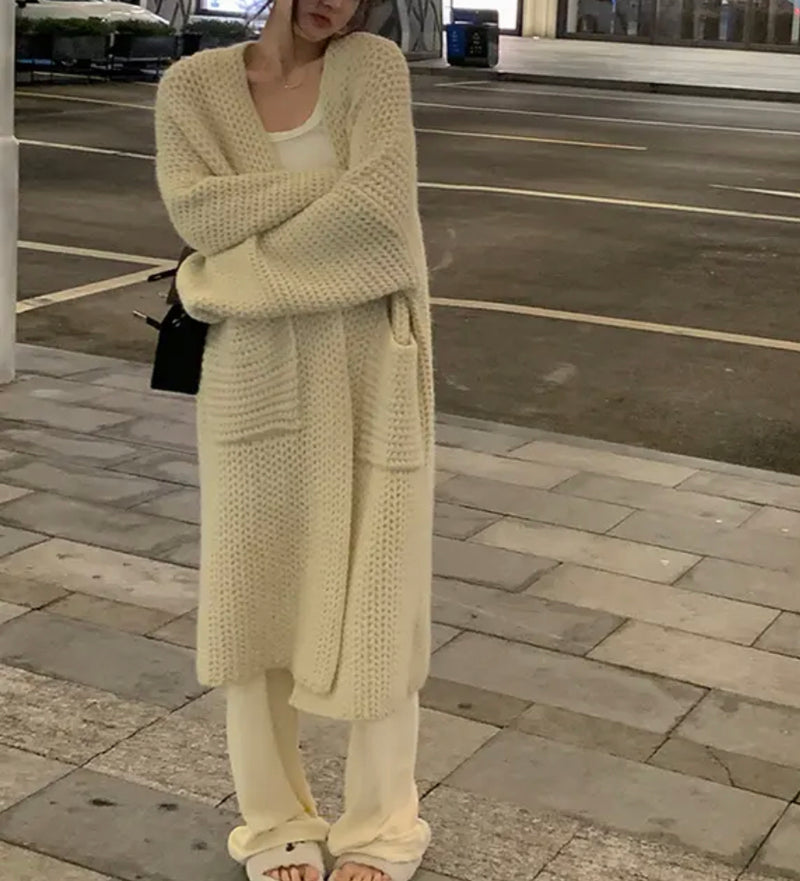 A woman wearing a cream sweater and pants stands on a sidewalk, showcasing the Knitted Long Cardigan.