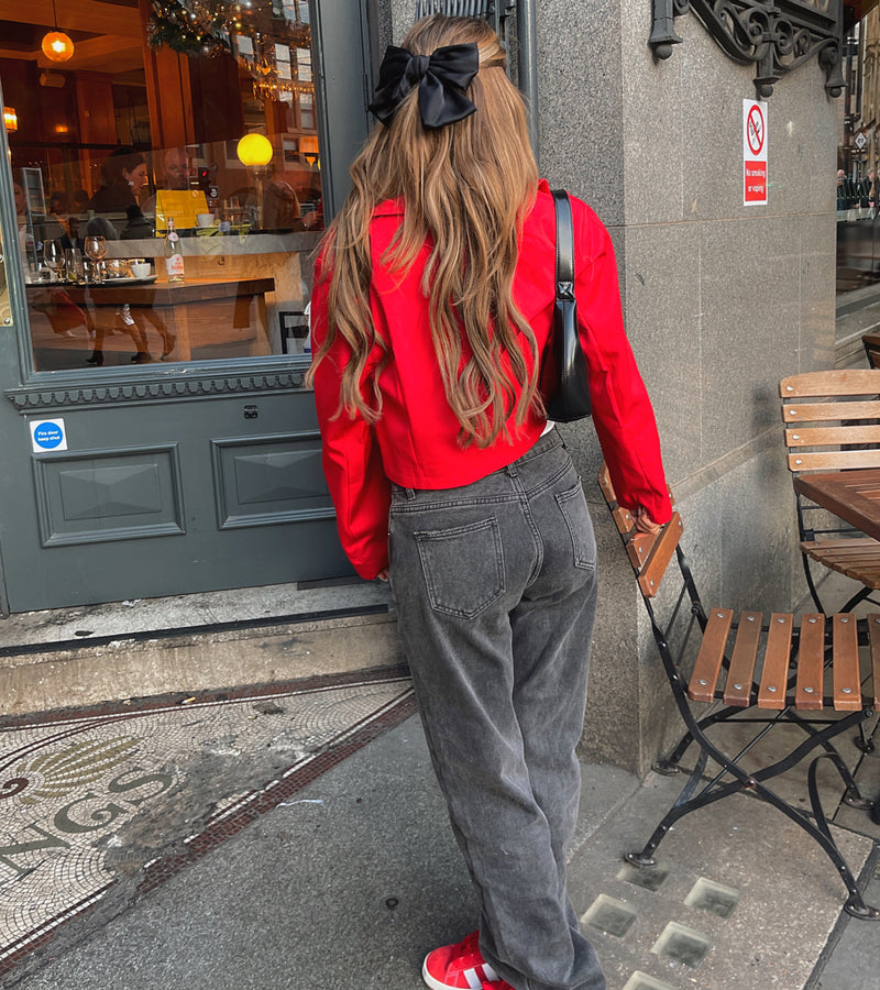  A woman wearing a red shirt and grey pants stands outside a cafe, showcasing the Crop Red Button Jacket