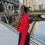 Fashionable woman wearing Crop Red Button Jacket, standing on a bridge in jeans.